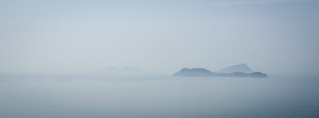 Distant islands appear through a soft morning haze over calm Seto Inland Sea waters, creating a serene and minimal seascape