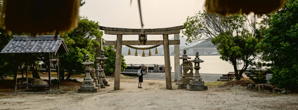 Cyclist photographing a seaside torii gate on Yumeshima Kaidō route
