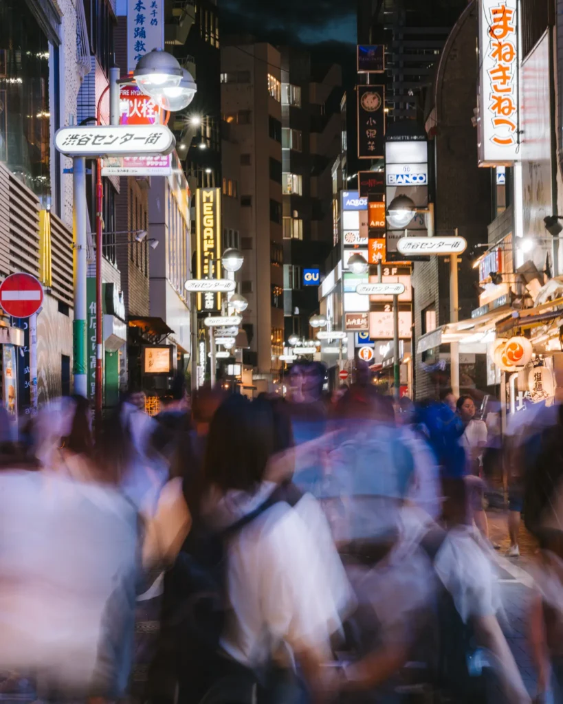 A crowded nighttime city scene with people blurred in motion