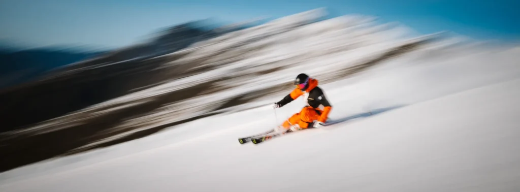 A skier in bright orange gear racing downhill, motion-blurred to convey speed, chaos, and loss of control