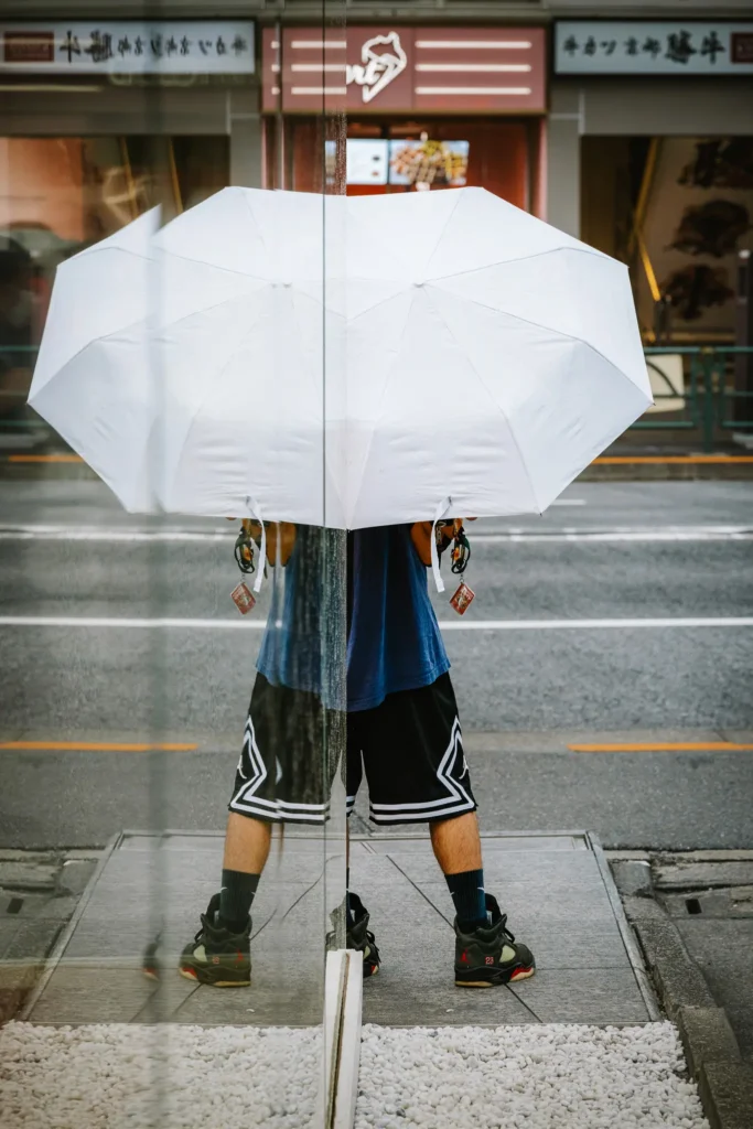 A half-visible person holding a white umbrella, reflected in glass so the same half appears mirrored, creating a disjointed, incomplete figure