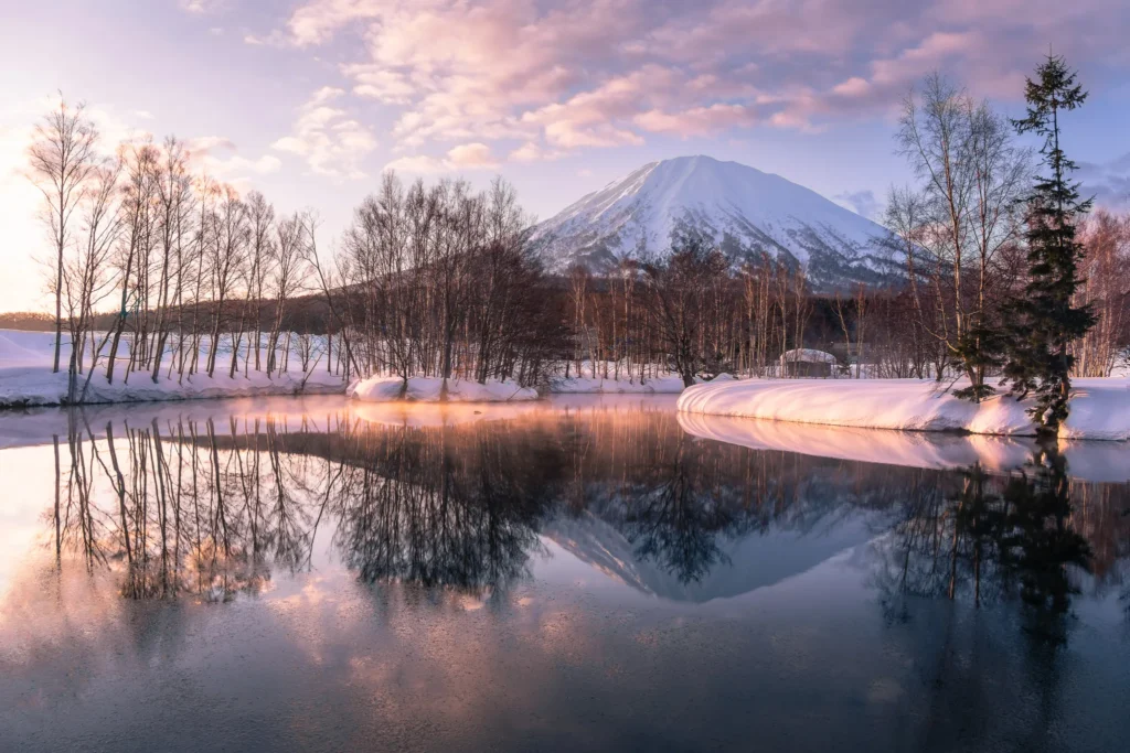 Mt. Yotei reflecting in a frozen lake at sunrise with soft winter light and snowy trees