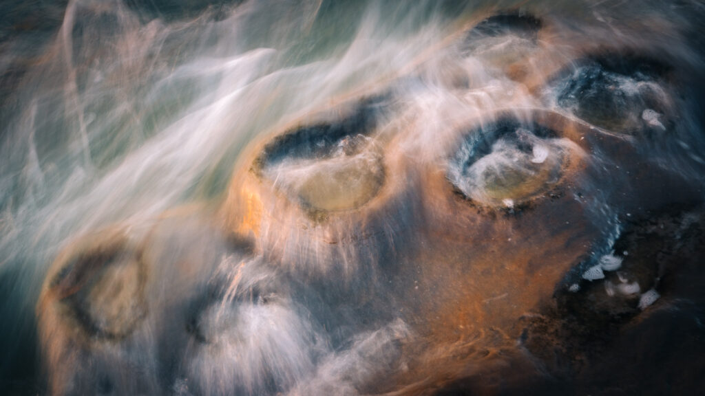 Long exposure of swirling waves over coastal rock pools, creating an abstract blend of motion and light.