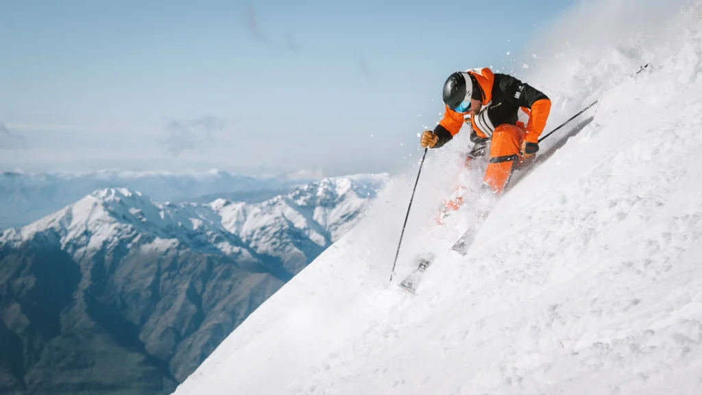 Ski photography example of skier in orange jacket turning on steep slope with mountains in the background, showing use of composition and angles.