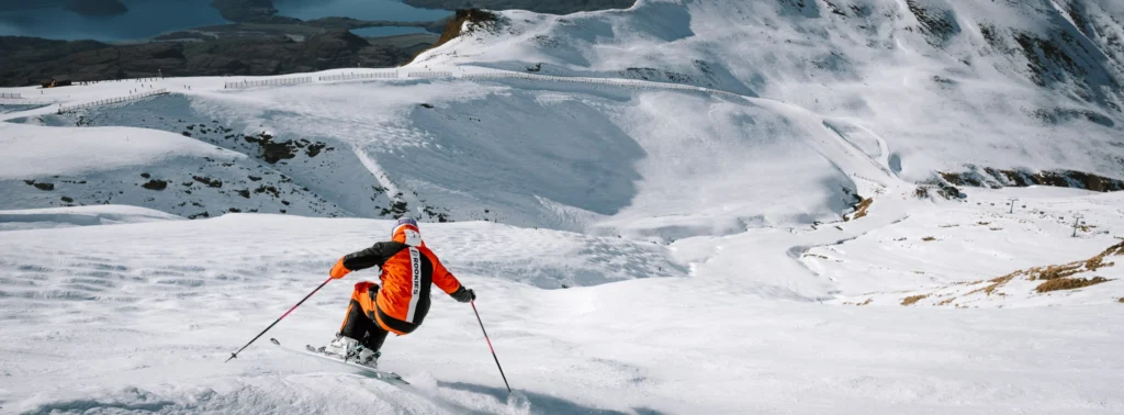 Wide ski photography example with skier in orange jacket descending a vast snowy mountain slope, highlighting storytelling through scale and environment.