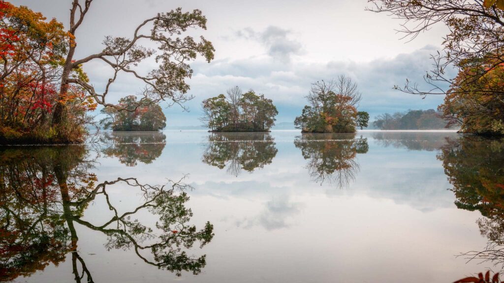 Small islands and a white bridge reflected on calm water at Lake Onuma in Hokkaido, Japan.