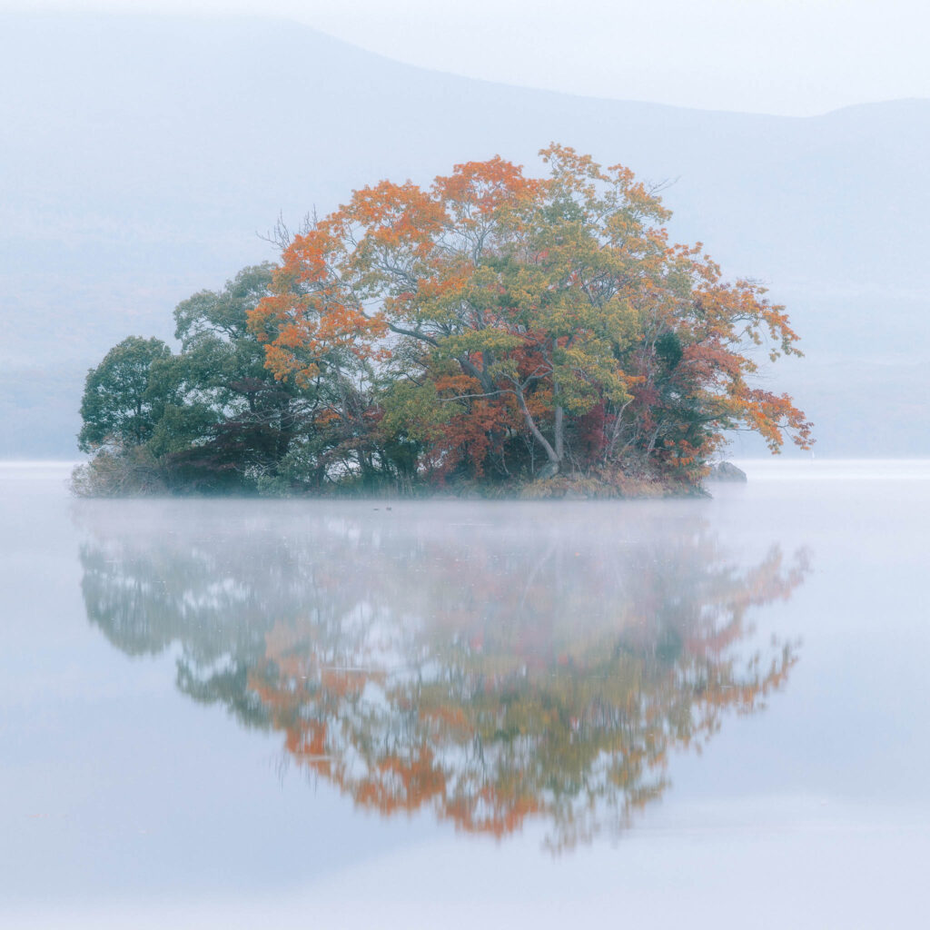 Small island reflected in calm misty water at Lake Onuma in Hokkaido, Japan.