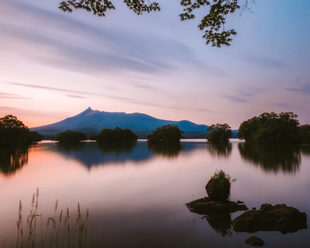 Mt. Komagatake reflected on calm water at Lake Onuma during early summer in Hokkaido, Japan.