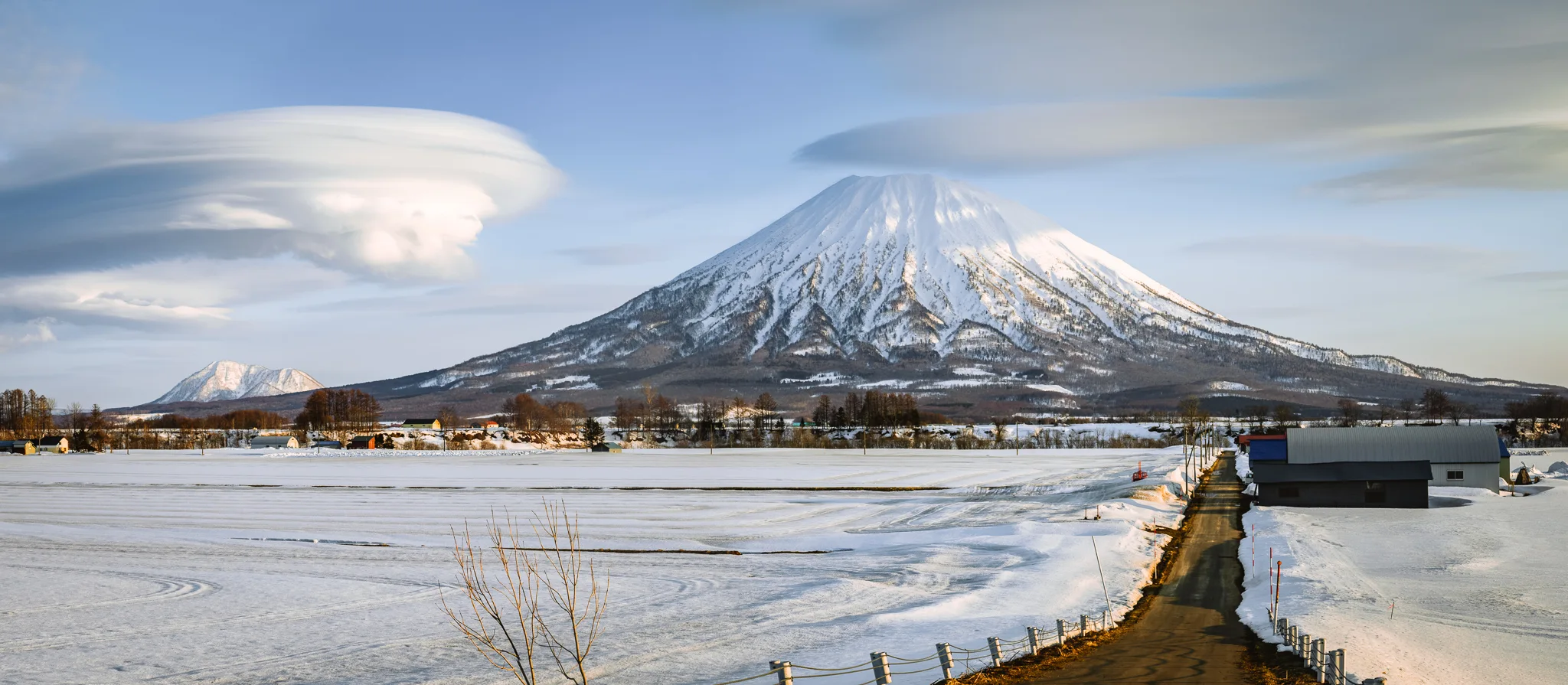 Mt Yotei rising above the snowy fields of Niseko, Hokkaido, Japan, under lenticular clouds at sunset.