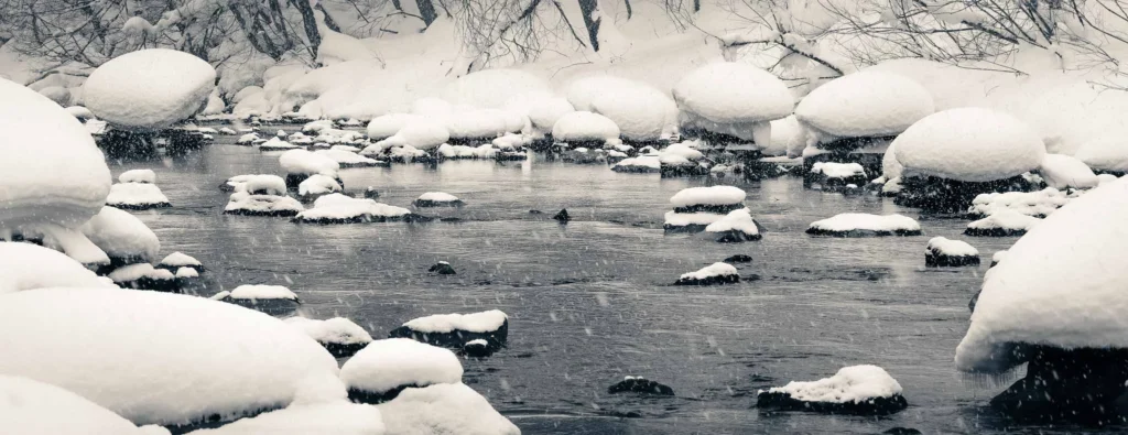 Snow-covered rocks shaped like mushrooms in a quiet winter river near Niseko, Hokkaido, Japan.