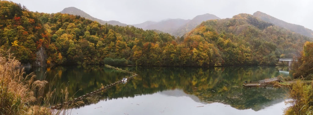Lake surrounded by steep autumn hills in Torizaki Valley in Hokkaido, Japan.