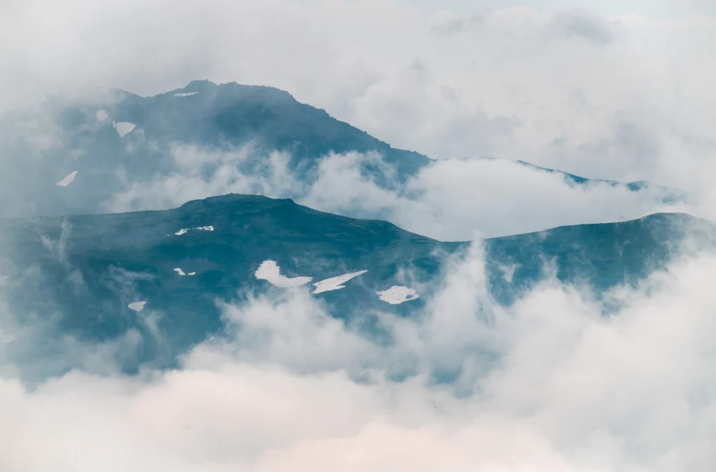 Clouds drift across layered volcanic peaks in the Daisetsuzan mountain range, seen from high elevation in central Hokkaido, Japan.