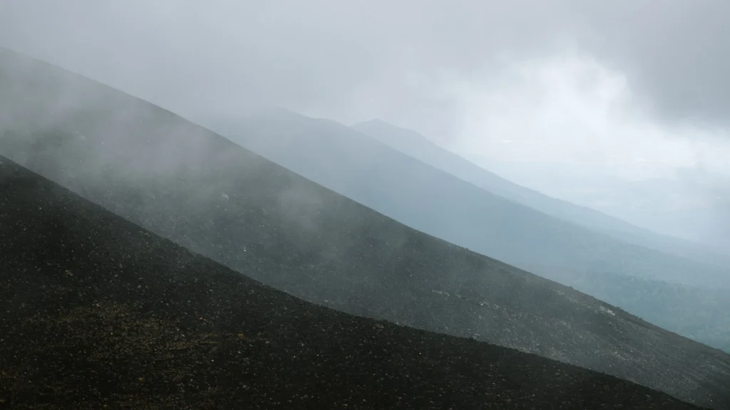 Mist drifts across steep volcanic slopes in the Daisetsuzan Mountains, with layered ridgelines fading into the distance in Hokkaido, Japan.