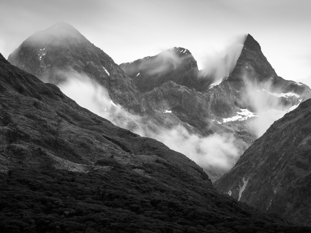 Long-exposure black and white image of New Zealand mountains with clouds sweeping across the peaks, showing how creative interpretation can shape a landscape photograph.