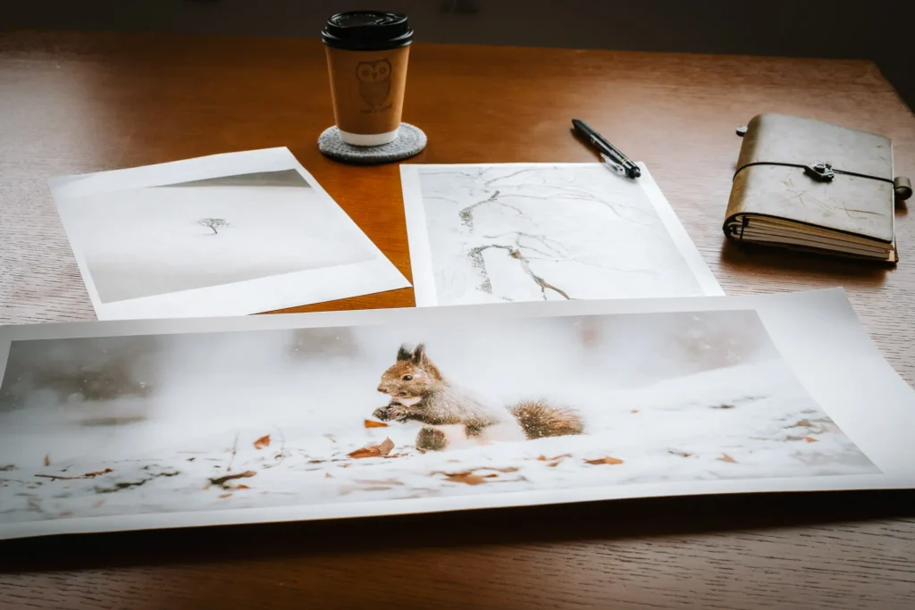 printing-photographs-mindful-photography-process Fine art photography prints laid out on a wooden desk alongside a notebook.