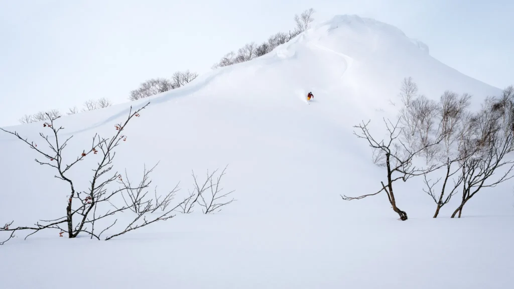 Skier descending a minimal snow-covered mountain slope with clean composition