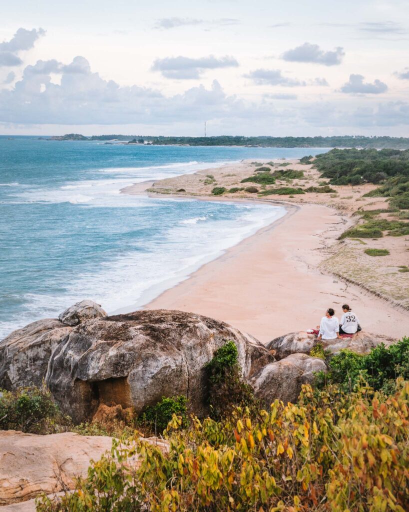 View from Elephant Rock near Arugam Bay, Sri Lanka, with rocks, beach, ocean and two people sitting above the coastline.
